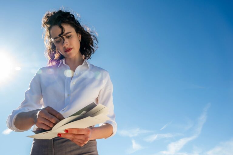 Margaret Qualley: Wearing a white shirt and gray pants. Holding papers as the sun shines…