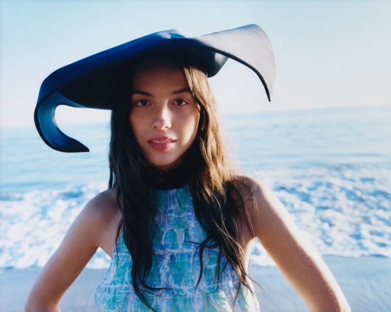 Olivia Rodrigo: Wears a large dark hat with a striking design. Dressed in a…