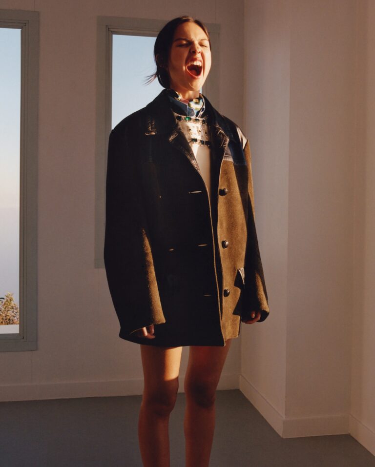 Olivia Rodrigo: Wearing an oversized dark coat that contrasts with a short dress that…