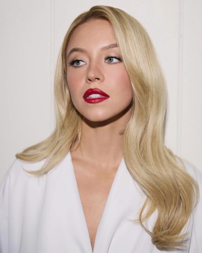 Sydney Sweeney: Cabello rubio largo y suelto, labios pintados de rojo brillante y maquillaje elegante. Lleva…