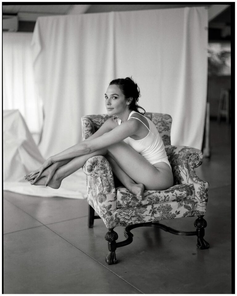 Gal Gadot: Sitting in a floral-print armchair, wearing a white bodysuit with no shoes. The…