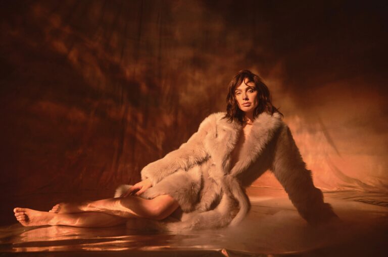 Gal Gadot: Wears a light fur coat, partially covering her body. No shoes, her…