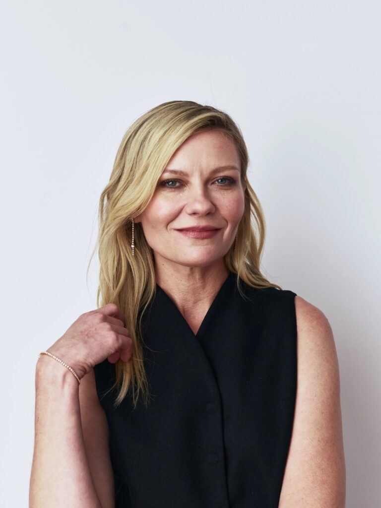Kirsten Dunst: Wears a black sleeveless vest with loose blonde hair. Wears a…