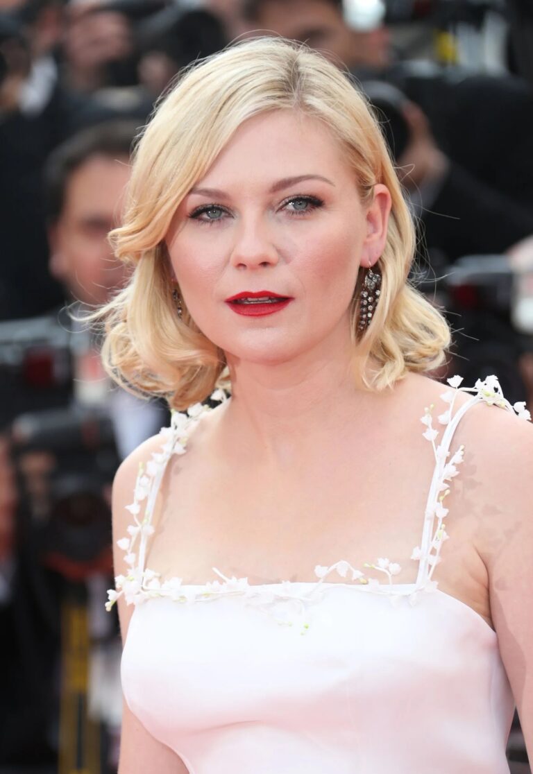 Kirsten Dunst: Wavy blonde hair, bold red lipstick. Wears a white dress…