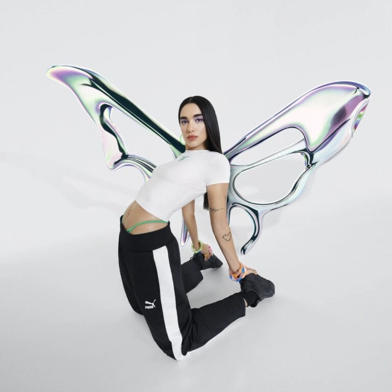 Dua Lipa: Luce una camiseta blanca ajustada y pantalones deportivos negros con franjas laterales, arrodillada en…