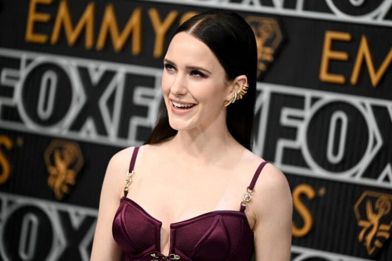 Rachel Brosnahan: Dressed in a purple top with structured details and delicate straps, highlighting a sophisticated silhouette.…