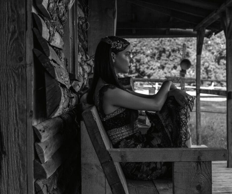 Anya Taylor-Joy: Posa sentada en un banco de madera, con un vestido largo de encaje negro…
