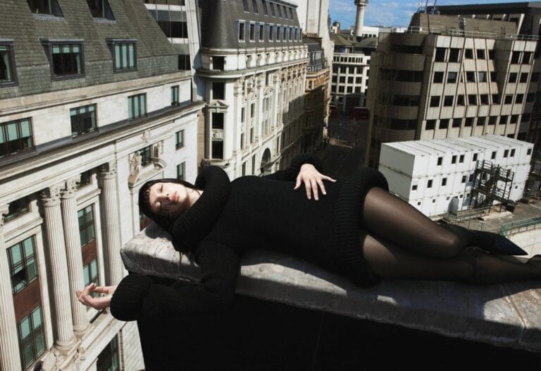 Dua Lipa: Aparece tumbada sobre el borde de un edificio, luciendo un suéter negro de gran…