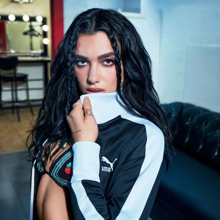 Dua Lipa: Luce una chaqueta deportiva negra con detalles en blanco, combinada con un sujetador brillante…