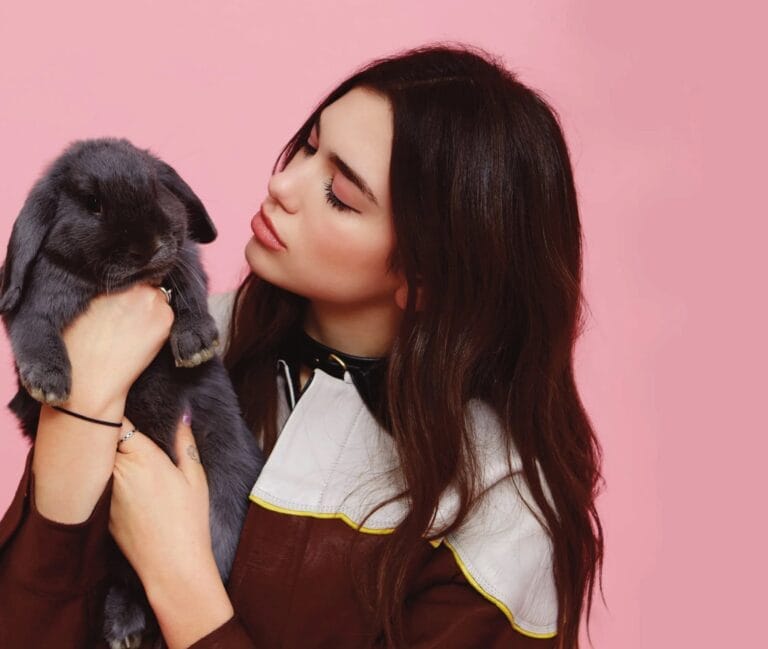 Dua Lipa: Luce una blusa marrón con un cuello blanco y detalles amarillos, sosteniendo con ternura…