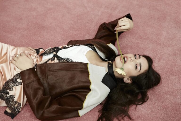 Dua Lipa: Aparece tumbada sobre una superficie rosa, luciendo un conjunto sedoso en tonos melocotón con…