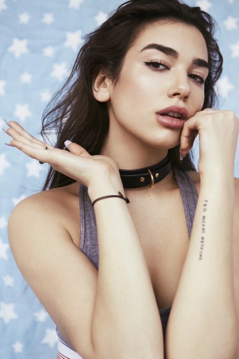 Dua Lipa: Luce una camiseta gris de tirantes que resalta su figura, complementada con un choker…