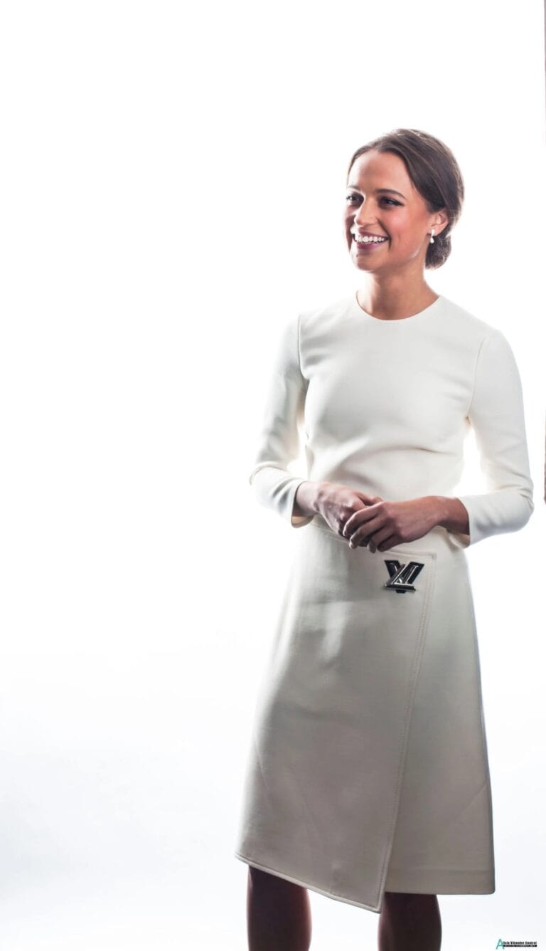 Alicia Vikander: Wears a clean-cut, elegant white dress with long sleeves and a…