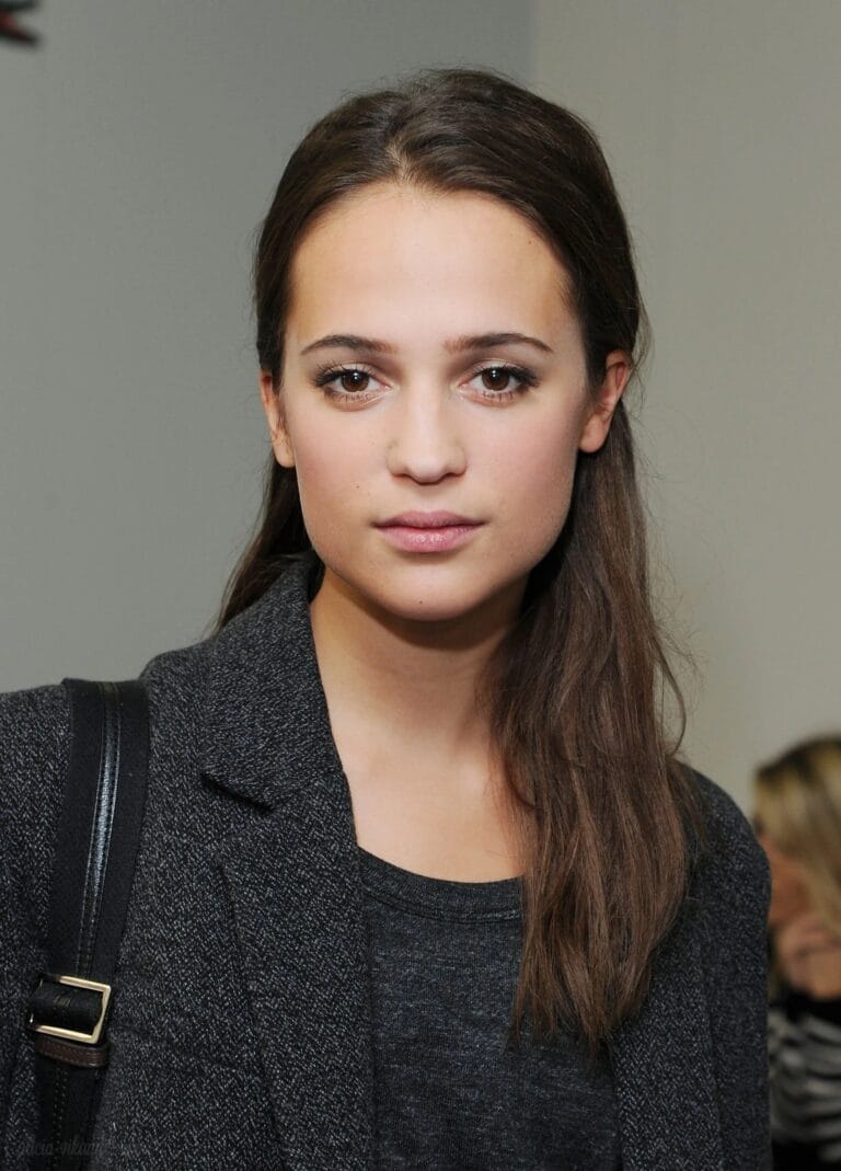 Alicia Vikander: Wears an elegant dark gray coat over a basic black T-shirt, creating a contrast…