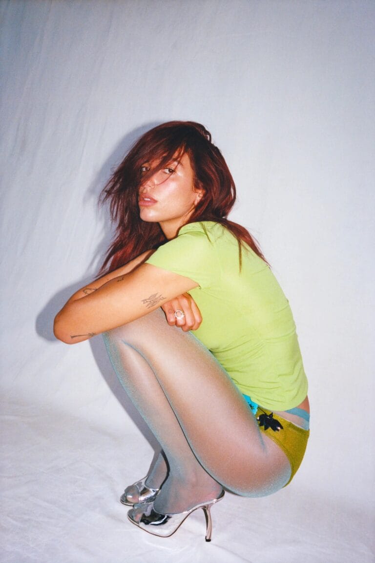 Dua Lipa: Luce una camiseta verde ajustada y shorts amarillos, mientras se encuentra en cuclillas sobre…