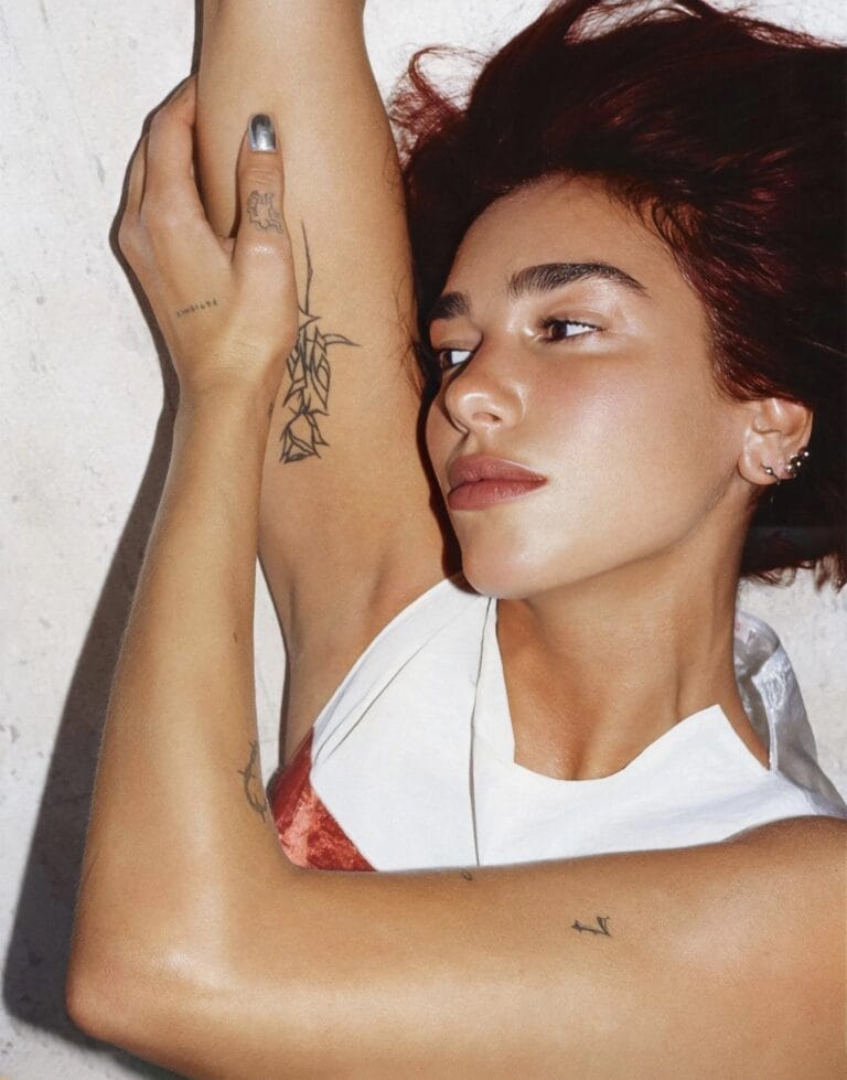 Dua Lipa: Luce una blusa blanca con detalles en terciopelo, reclinada sobre una superficie clara, con…