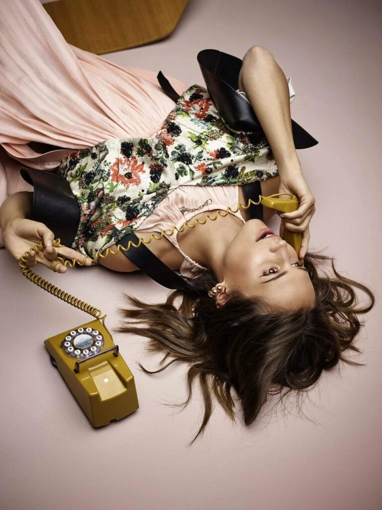 Alicia Vikander: Lying on a pink background, wearing a pastel-toned dress and a…