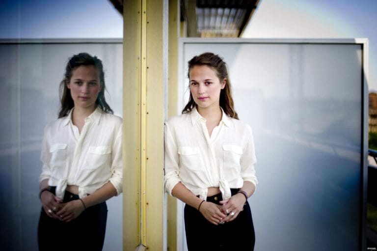 Alicia Vikander: Wears a loose white blouse tied at the waist, which highlights her…