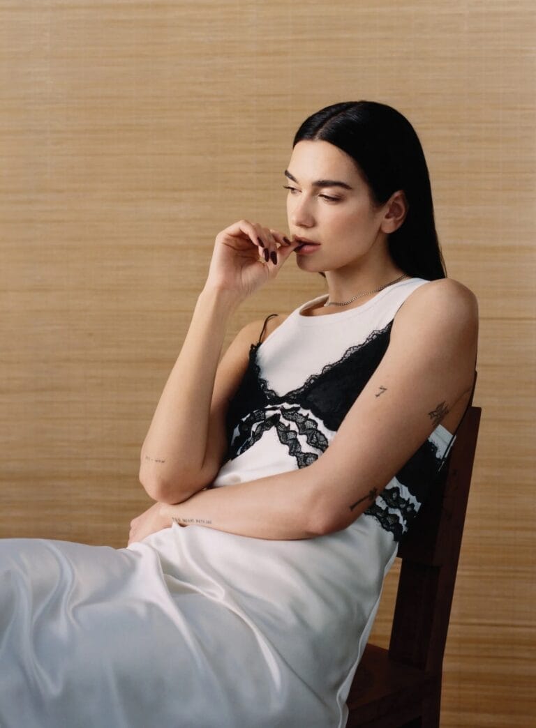 Dua Lipa: Luce un vestido de seda blanco con detalles de encaje negro, sentado en una…