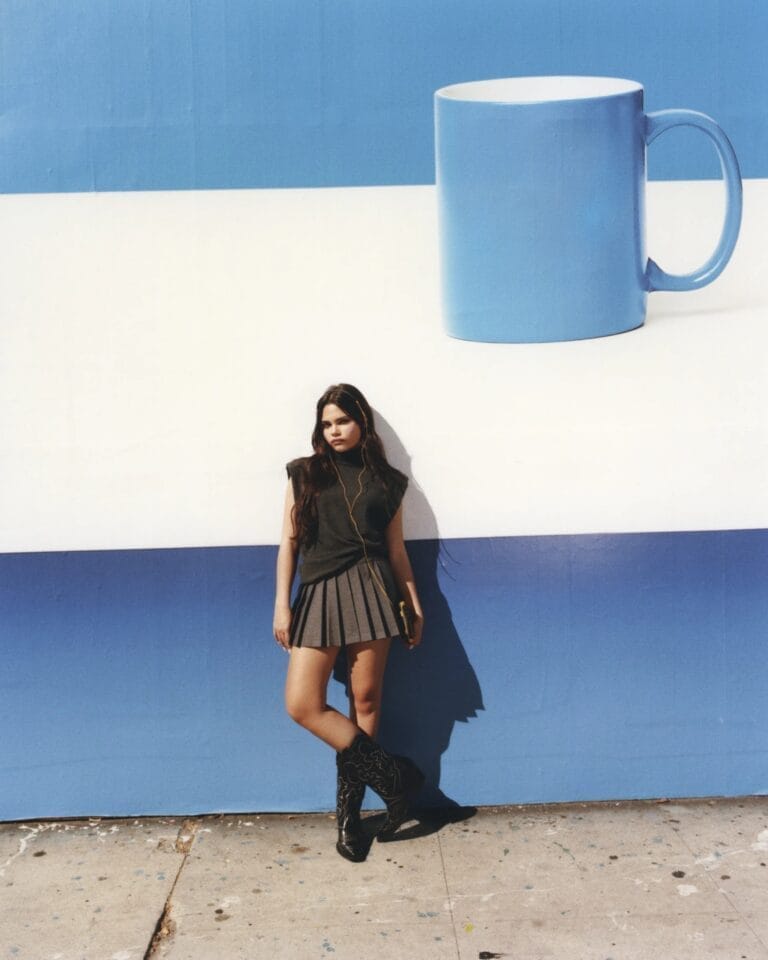 Ariana Greenblatt: Poses leaning against a blue-toned wall, wearing a sleeveless gray top…