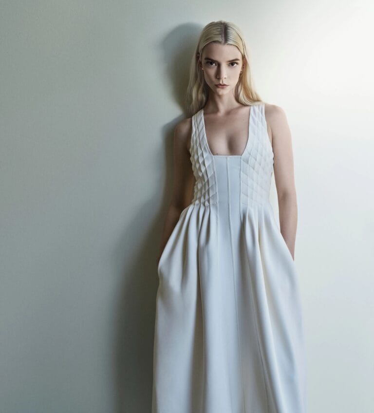 Anya Taylor-Joy: Wears a white flowing dress with pleated details at the neckline that…