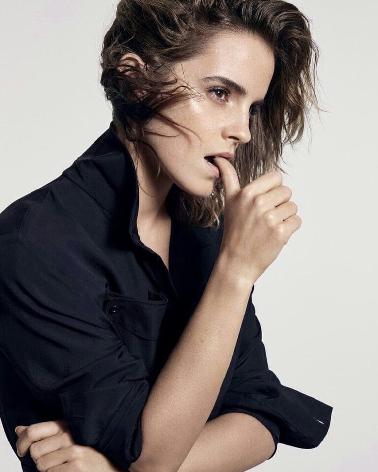 Emma Watson: Luce una camisa negra de corte contemporáneo, con las mangas ligeramente arremangadas, mientras sujeta…