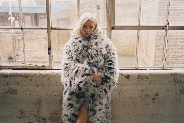 Anya Taylor-Joy: Wears a gray and black fur coat, wrapping and soft in texture, while…