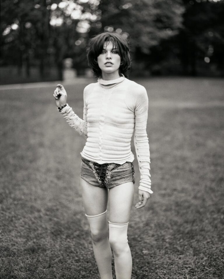 Milla Jovovich: Luce un suéter ajustado y transparente de manga larga, combinado con shorts cortos de…
