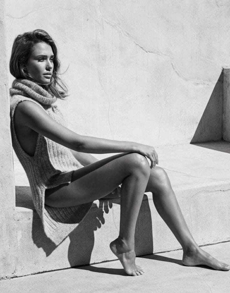 Jessica Alba: She wears a sleeveless knit sweater with a large collar. She is barefoot and…