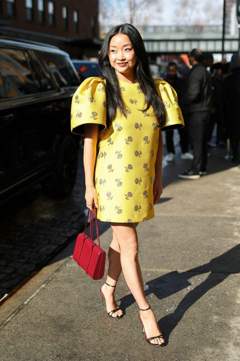 Lana Condor: Wears a yellow dress with puff sleeves and a delicate floral print, walking…