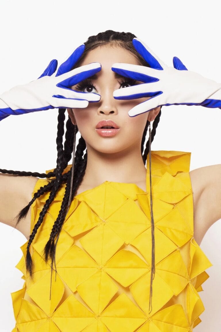 Lana Condor: Wears a structured yellow dress with a geometric design that flatters her figure. Holds…