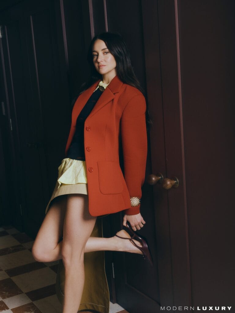 Shailene Woodley: Wears a structured red coat over a dark blouse with a detail on the…