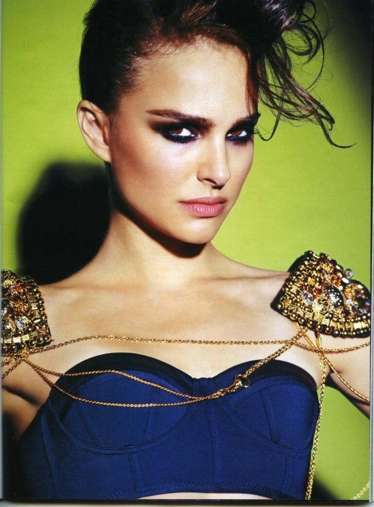 Natalie Portman: Wears a dark blue top with structured details, adorned with gold chains that fall…