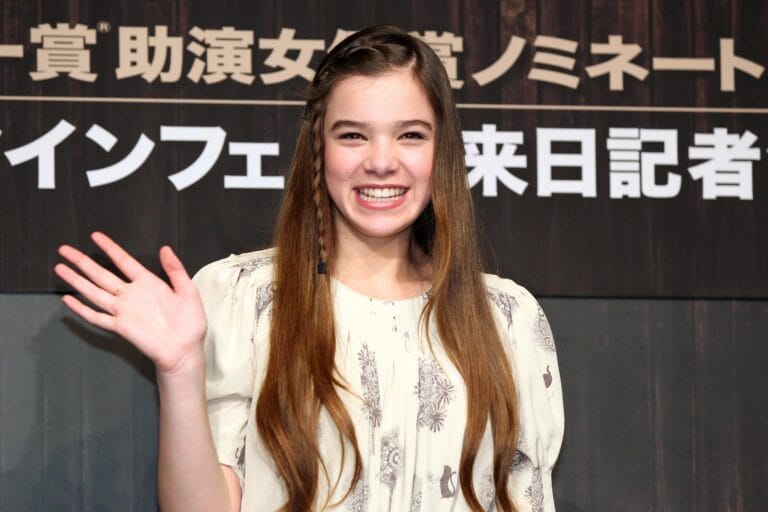 Hailee Steinfeld: Luce una blusa clara con estampados delicados, sonriendo y levantando la mano en un…