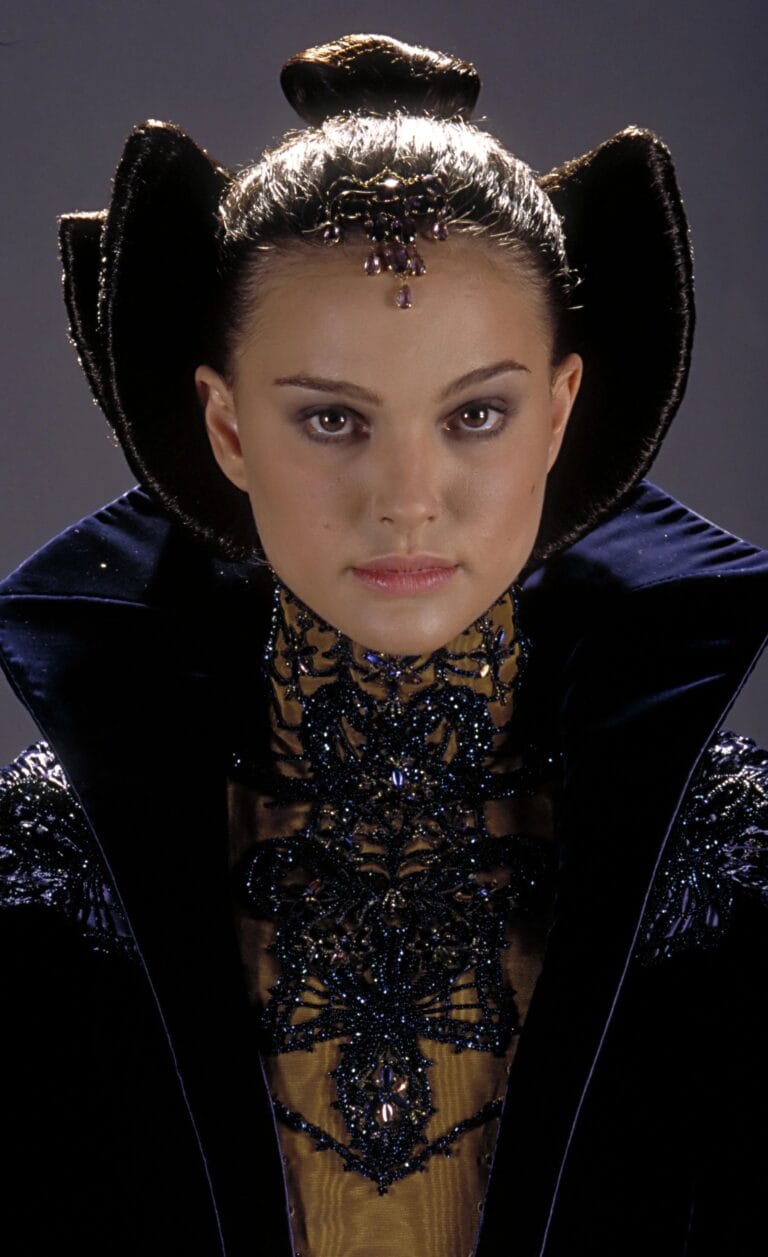 Natalie Portman: Wears a dramatic outfit with a high collar and intricate embroidery in dark tones,…