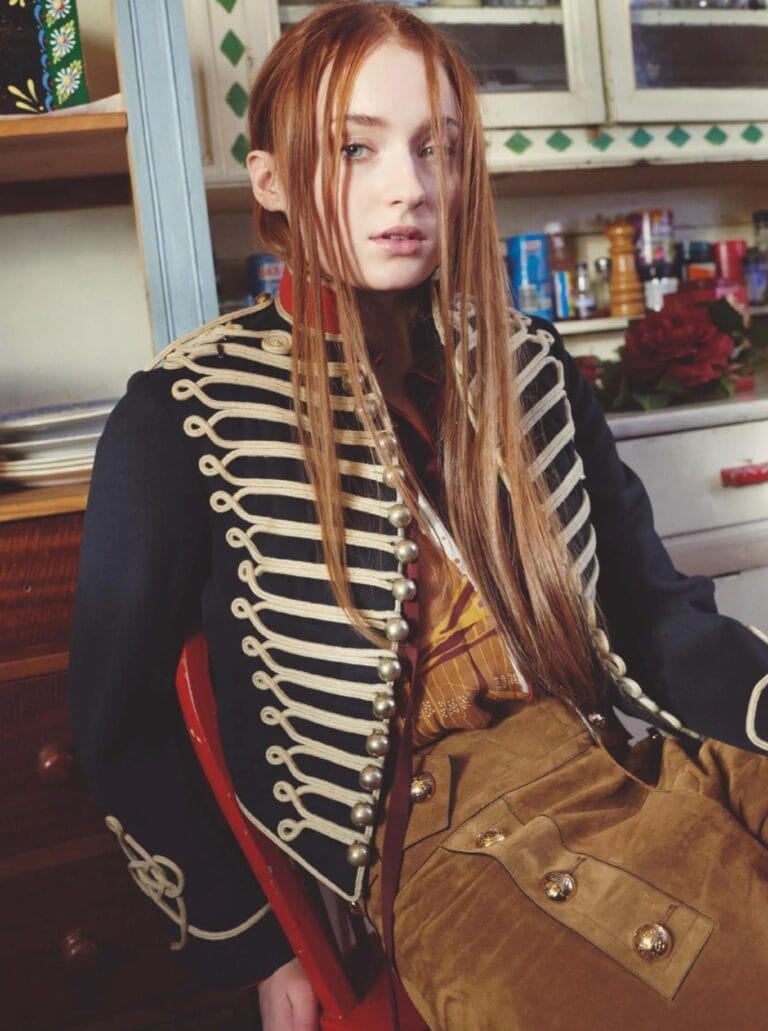 Sophie Turner: Wears a black military jacket with gold details and prominent buttons, paired with…