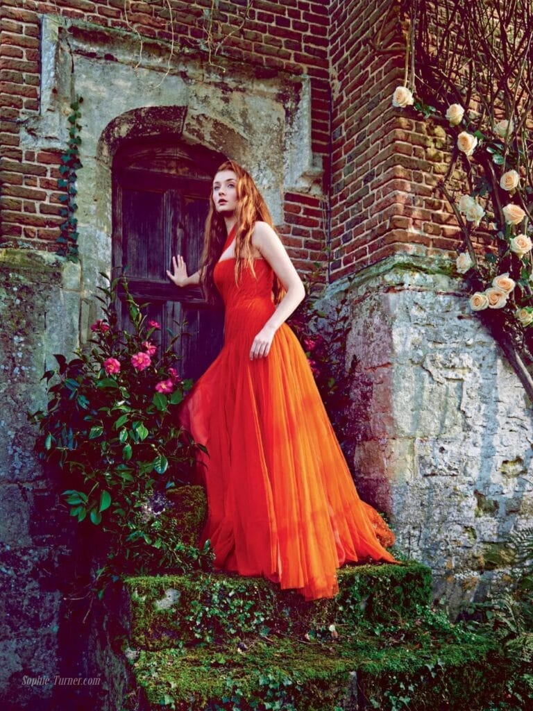 Sophie Turner: Wears a long, flowing dress in vibrant orange that contrasts with…