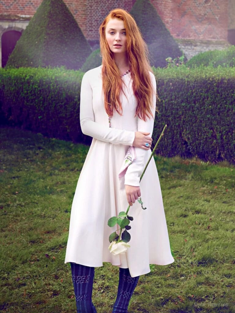 Sophie Turner: Wears a long, flowing white dress with long sleeves and details…