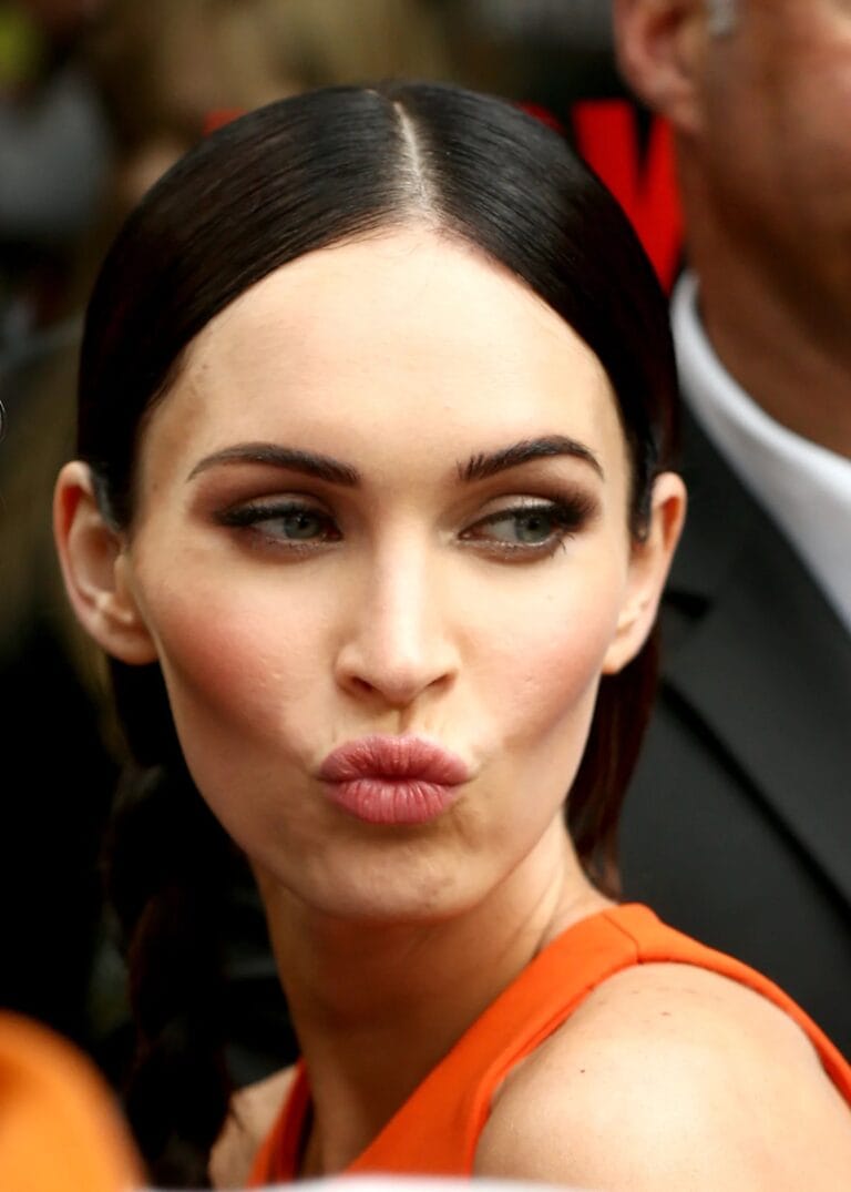 Megan Fox: Wears a sleeveless orange dress that highlights her figure while making a gesture…