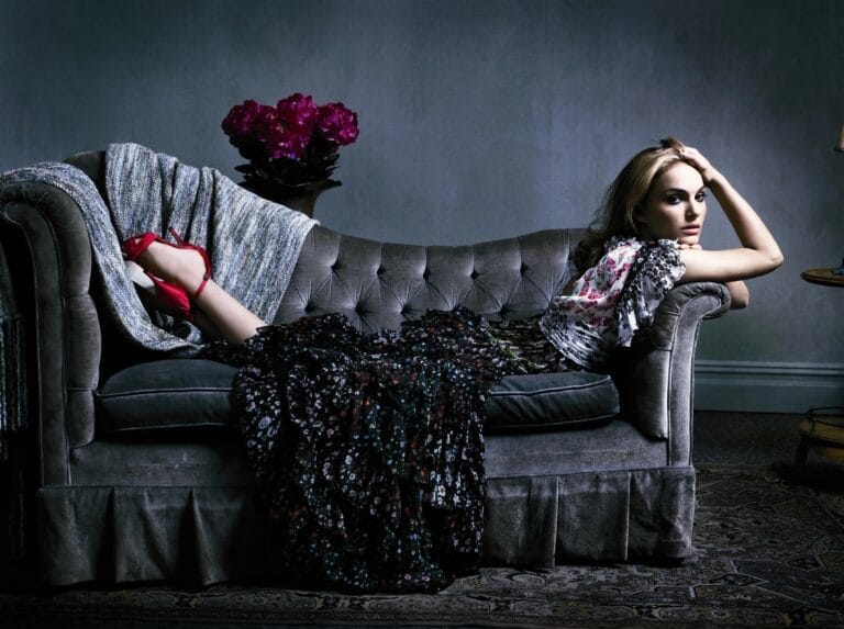 Natalie Portman: Wears a long dress with dark floral print, gracefully draped over a gray sofa.…