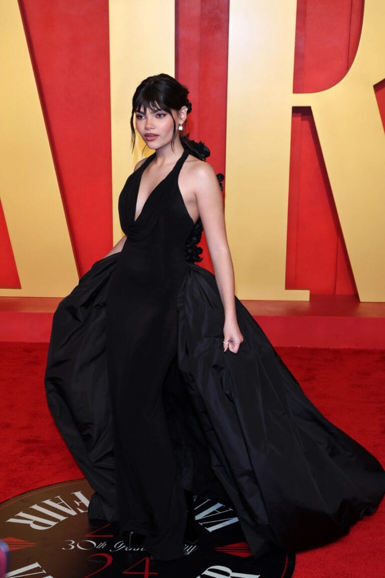 Ariana Greenblatt: Wears an elegant long black dress with a deep neckline that…