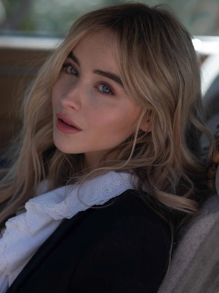 Sabrina Carpenter: Luce una blusa negra con un voluminoso cuello de encaje blanco, que aporta un…
