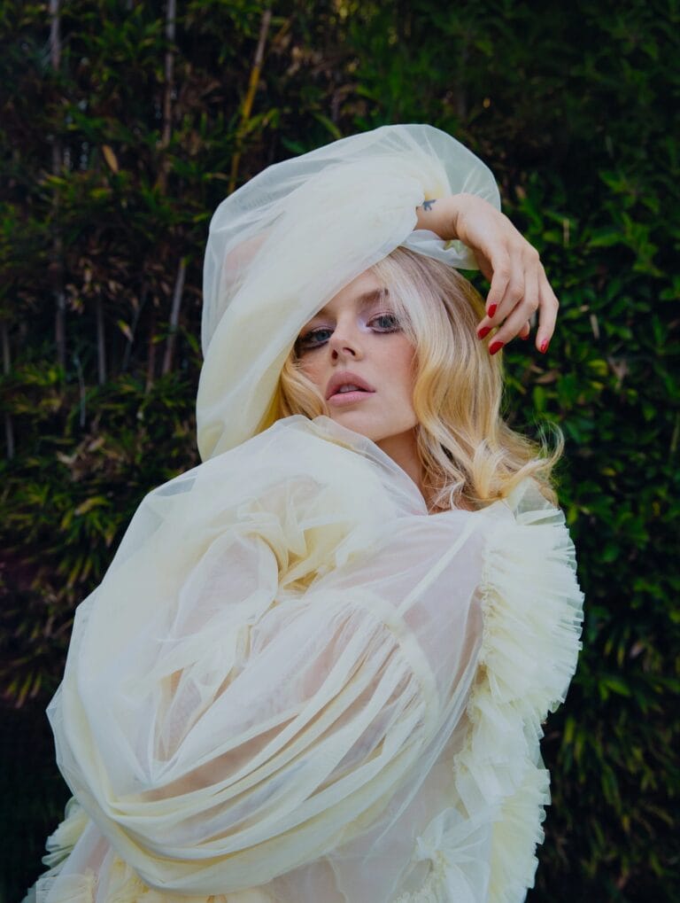 Samara Weaving: Wears a white organza blouse with delicate ruffles, playing with the light…