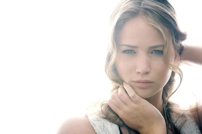 Jennifer Lawrence: Wears a light top with a soft texture, highlighting her figure while holding her hair…