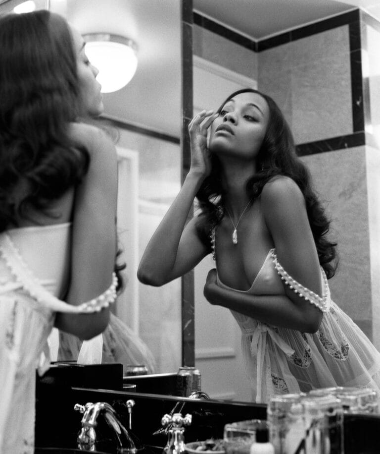 Zoe Saldaña: Poses in a delicate, semi-sheer white lace robe while looking at herself in the mirror.…