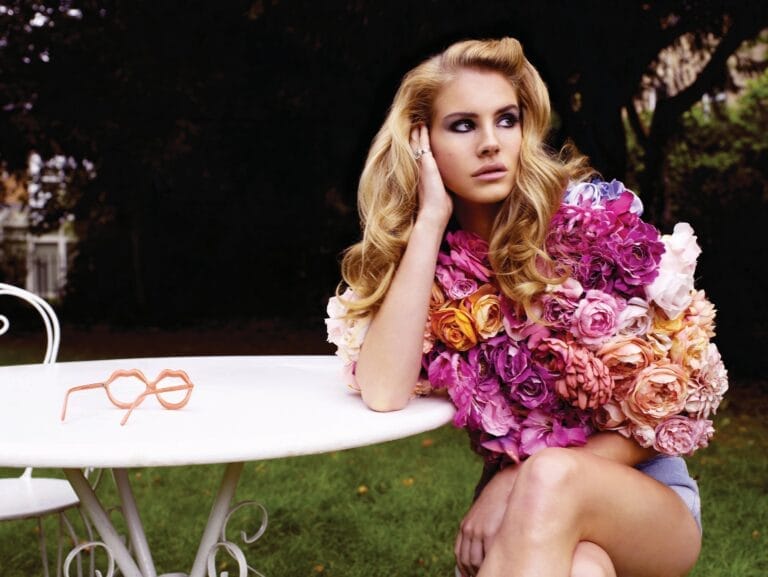 Lana Del Rey: Luce un impactante abrigo de flores en tonos rosas y naranjas, sentado en una…