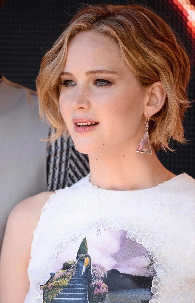 Jennifer Lawrence: Wears a white top with an artistic design on the front, which highlights her…