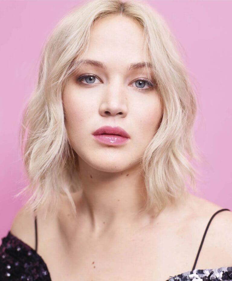 Jennifer Lawrence: Wears a glossy black top with sequin details, while the pink background highlights…