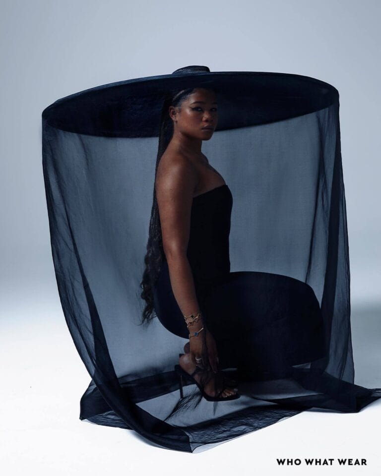 Storm Reid: Wears a fitted black sleeveless dress, posing on her knees under a large…