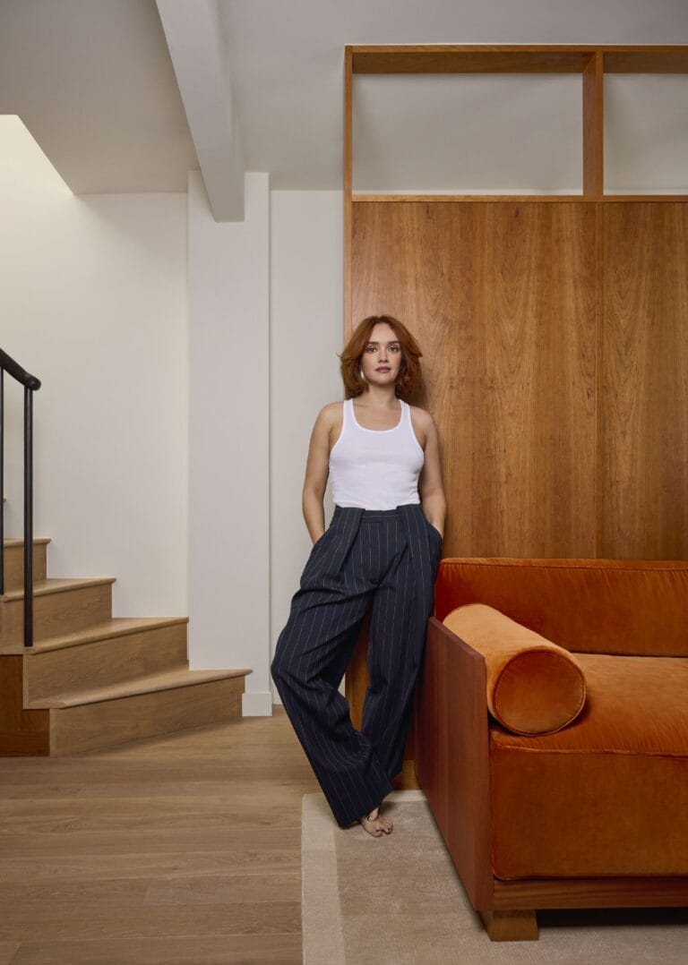Olivia Cooke: Wears a white sleeveless top and navy blue pleated trousers with stripes,…